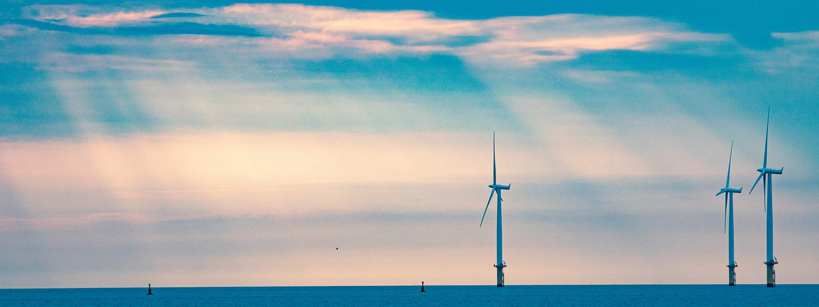 The sun shining through clouds over wind turbines at sea